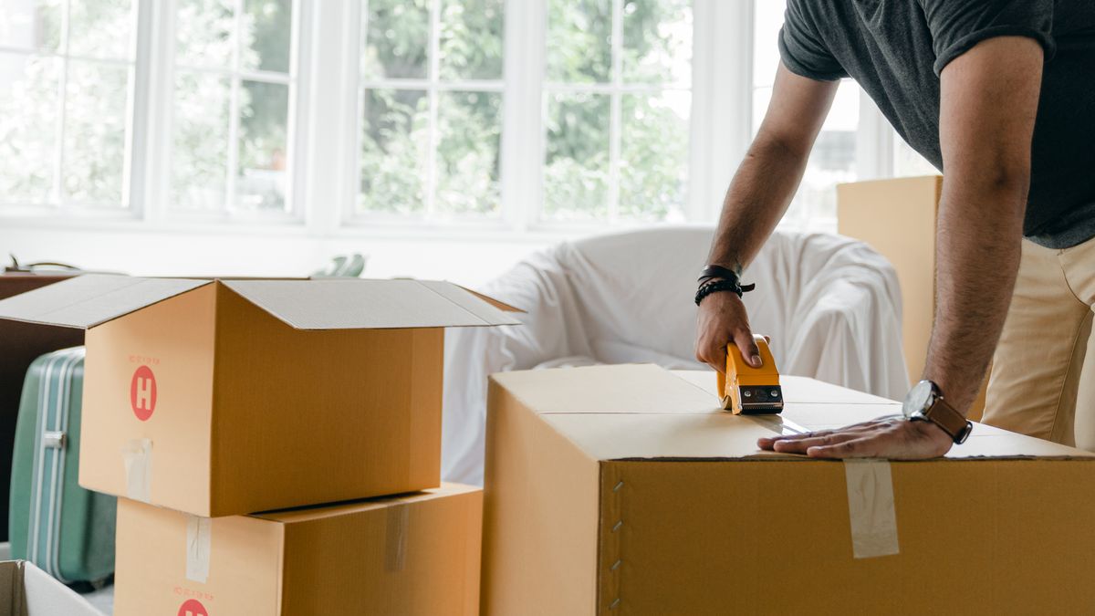 Hands taping a cardboard moving box shut during packing