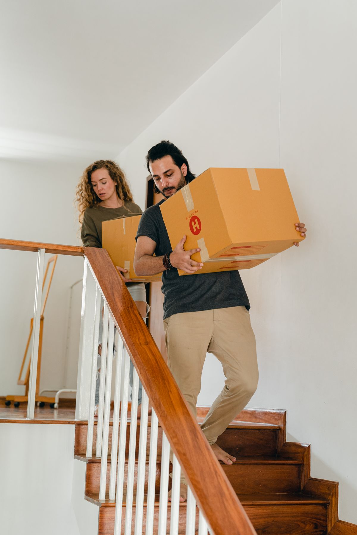 A couple carrying moving boxes down an apartment staircase