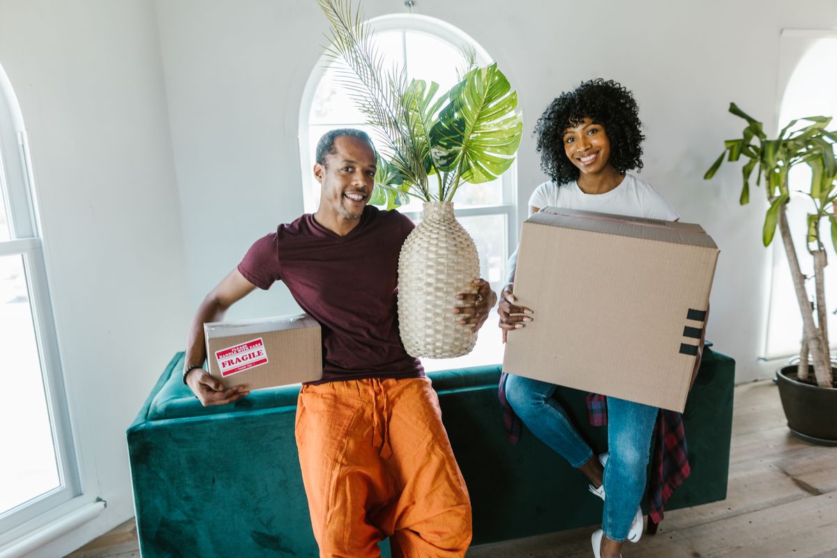 A couple carrying boxes and a plant into their new home